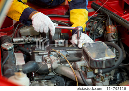 Closeup mechanic hand in work uniform, working on a car in an automotive shop or garage. He seem focused and engaged in diagnosing or repairing the vehicle's engine or other component. Closeup mechanic hand in work uniform, working on a car in an automotive shop or garage. He seem focused and engaged in diagnosing or repairing the vehicle's engine or other component. 114792116