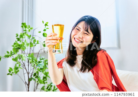 一名 20 多歲到 30 多歲的年輕女子在假期的明亮時間裡在家中的房間裡喝著啤酒。 一名 20 多歲到 30 多歲的年輕女子在假期的明亮時間裡在家中的房間裡喝著啤酒。 114793961