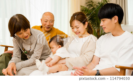 Smiling and happy multi-generational family being held by mother on sofa and getting attention from family 114794030
