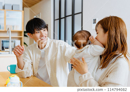 A mother holds her baby in her living room at home while her smiling father watches A mother holds her baby in her living room at home while her smiling father watches 114794082