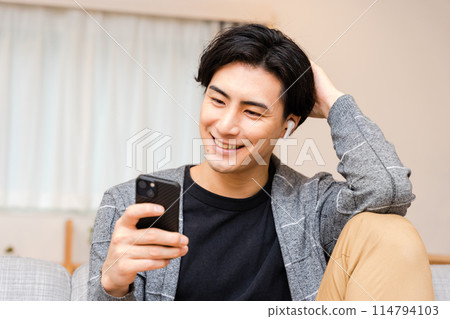 Smiling man in his 30s listening to music on his smartphone and talking with a friend using wireless earphones 114794103