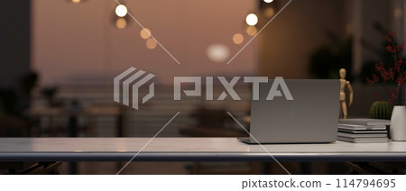 A computer on a tabletop with a blurred background of a beautiful sunset view through the balcony. 114794695