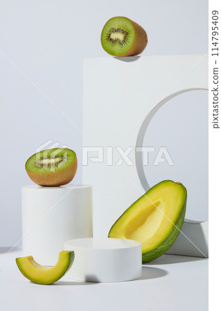 Frontal shot photo on white background with white blank pedestal for displaying cosmetic or hair care products extracted from avocado and kiwi ingredient. Blank space for advertising 114795409
