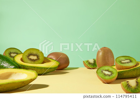Creative template for design with front shot, a countertop of yellow color covered by fresh kiwi and avocado over green background. Vacant space in center for showing product has natural origin 114795411