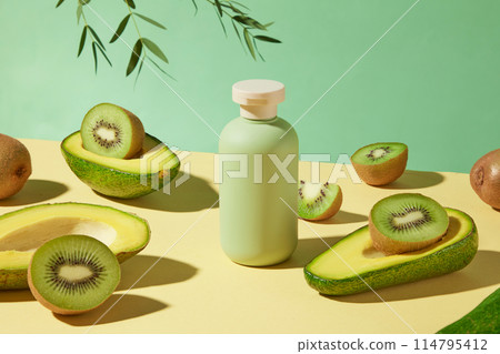 Unique photograph for advertising, a yellow table top displaying a blank cosmetic bottle of green color, avocado and kiwi neatly arranged around. Blank space for design with front shot 114795412