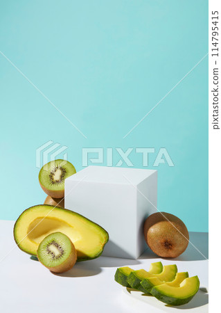 The blank podium in rectangular shape placed in the center over baby blue background, fresh avocado and kiwi decoration around. Photo was shot from front, vacant space for promotion 114795415