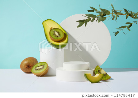 The blue background highlights white color of blank circular platforms, decorated with the green of kiwis and tree branches, and the yellow color of fresh avocados. Advertising photo with copy space The blue background highlights white color of blank circular platforms, decorated with the green of kiwis and tree branches, and the yellow color of fresh avocados. Advertising photo with copy space 114795417