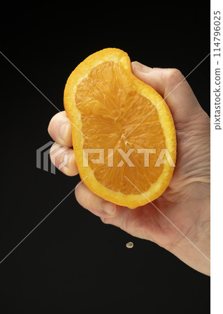 Squeezing an orange on a black background Squeezing an orange on a black background 114796025