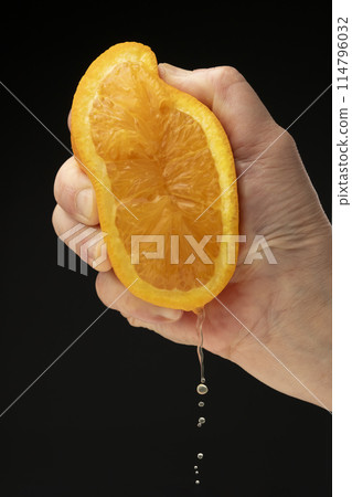 Squeezing an orange on a black background Squeezing an orange on a black background 114796032