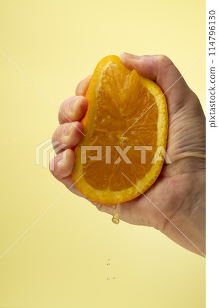 Squeezing an orange on a yellow background Squeezing an orange on a yellow background 114796130