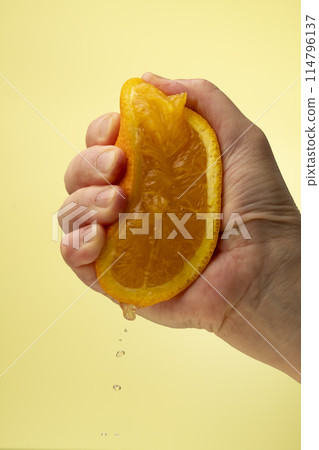Squeezing an orange on a yellow background Squeezing an orange on a yellow background 114796137