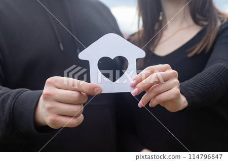 A young couple shows a house with a heart inside. 114796847