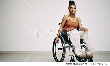 Young disabled African American woman in wheelchair against white wall 114797237