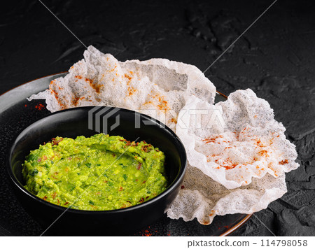 Fresh guacamole with rice chips on dark plate 114798058