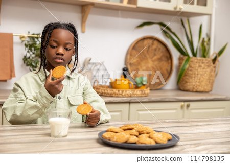 Joyful little girl enjoying delicious snack at home drinking milk with cookies 114798135
