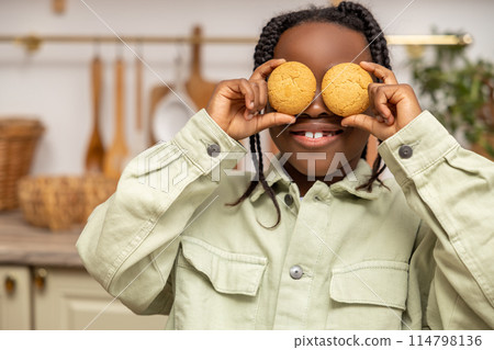 Cheerful multicultural little girl enjoying cookies and milk during breakfast 114798136