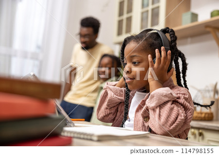 African American child siting at table completing her schoolwork with the help of her digital tablet 114798155
