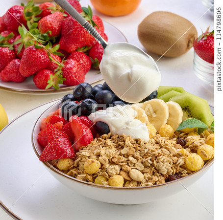 Granola with strawberries, kiwi, banana and blueberries in a round plate topped with yogurt on the table. Healthy and tasty food 114798606