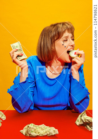 Portrait of young girl with makeup holding dollar money, crying and eating onion against vivid yellow background. Cost of Living Tears 114798621