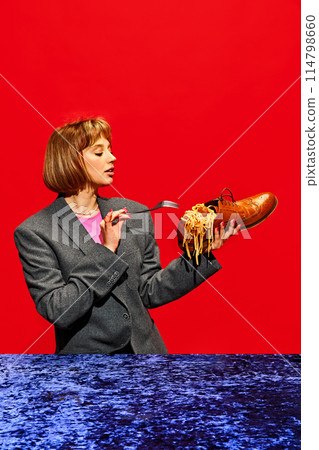 Creative image of woman eating spaghetti served in leather shoe against red background. Fashion and food mixed in unexpected way. 114798660