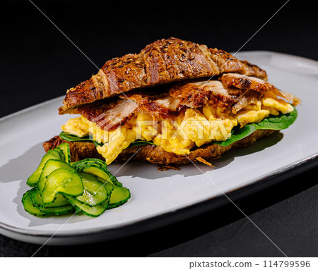 Delicious croissant sandwich with scrambled eggs, bacon, and avocado on a plate Delicious croissant sandwich with scrambled eggs, bacon, and avocado on a plate 114799596