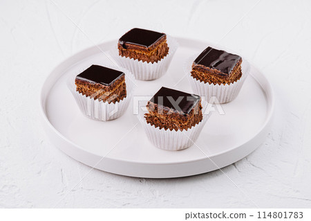 Chocolate glazed mini cakes on white plate Chocolate glazed mini cakes on white plate 114801783