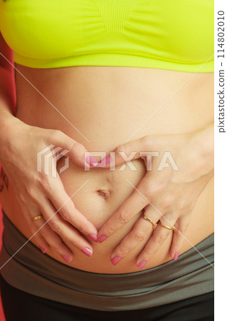 pregnant woman making heart shape with hands over belly 114802010
