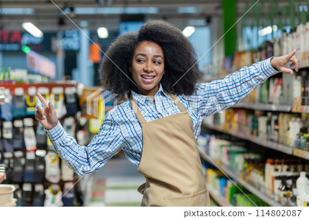 An enthusiastic grocery store employee in a checked apron and shirt cheerfully poses in the aisle surrounded by products, creating a positive work environment with a happy 114802087
