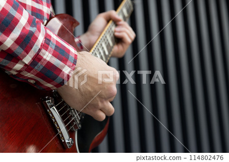 A stylish young guy plays the guitar on a dark background 114802476