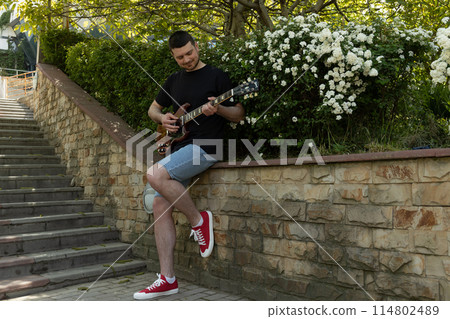 Attractive young guy playing guitar in the park Attractive young guy playing guitar in the park 114802489