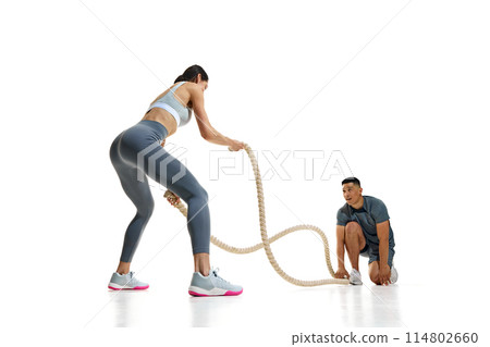 Dynamic photo of athletic woman and man engaged in workout with battle ropes against white studio background. Dynamic photo of athletic woman and man engaged in workout with battle ropes against white studio background. 114802660