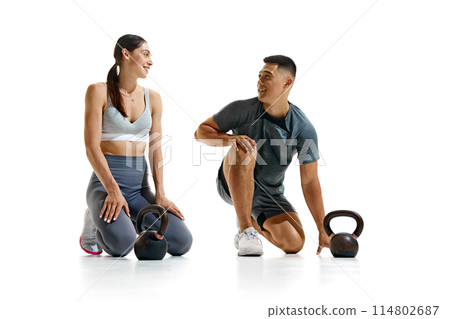 Portrait of man and woman taking break from their workout, kneeling on floor and smiling at each other against white studio background. 114802687