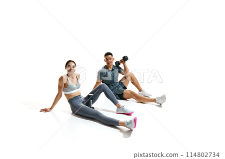 Man and woman wearing sport uniform sitting on floor, taking break from their workout against white studio background. 114802734