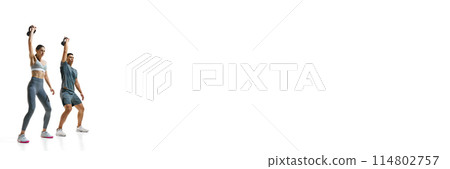 Banner. Man and woman dressed sportwear in mid-exercise, each holding kettlebell aloft with one arm against white studio background. Banner. Man and woman dressed sportwear in mid-exercise, each holding kettlebell aloft with one arm against white studio background. 114802757