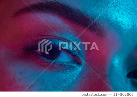 Close-up photo of female eye, highlighting well-defined eyebrow, long eyelashes, and smooth skin in neon light. Close-up photo of female eye, highlighting well-defined eyebrow, long eyelashes, and smooth skin in neon light. 114802805