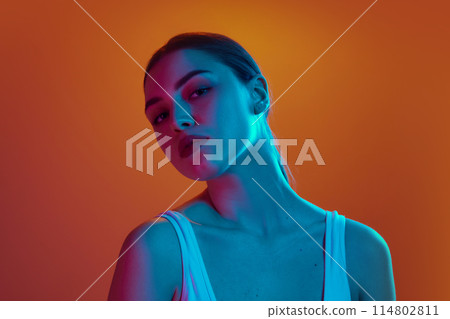 Portrait of sensual young woman with long, dark hair posing looking at camera in neon light against gradient background. Portrait of sensual young woman with long, dark hair posing looking at camera in neon light against gradient background. 114802811