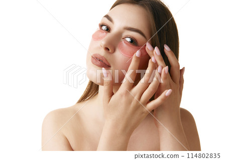 Skincare routine. Beautiful brunette woman applying pink hydrogel patches under her eyes against white studio background. 114802835
