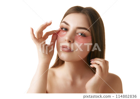 young woman looks fresh and well-cared-for with minimal makeup and with hydrogel eye patches against white background. 114802836