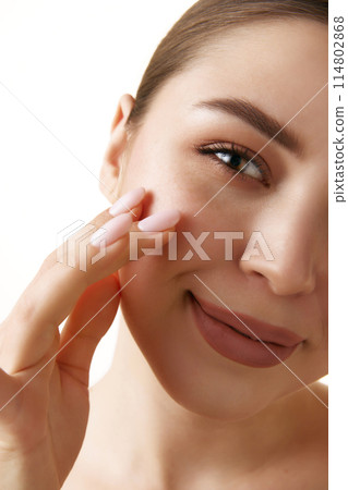 Close-up photo of young brunette woman with moisturized, smoothy skin and neutral make up touches skin against white background. Close-up photo of young brunette woman with moisturized, smoothy skin and neutral make up touches skin against white background. 114802868