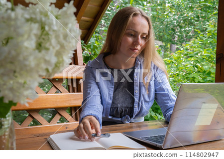 Female student has online lesson education outdoor in garden wooden alcove. Blonde woman sitting outside work on laptop having video call Female student has online lesson education outdoor in garden wooden alcove. Blonde woman sitting outside work on laptop having video call 114802947