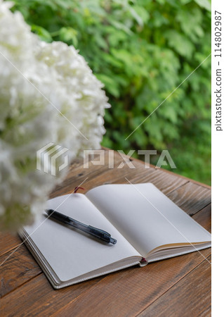 Open white empty paper notepad on wooden table outdoors. Concept of author writing in relaxed cozy atmosphere. Spiritual health digital detox slowing down Open white empty paper notepad on wooden table outdoors. Concept of author writing in relaxed cozy atmosphere. Spiritual health digital detox slowing down 114802987