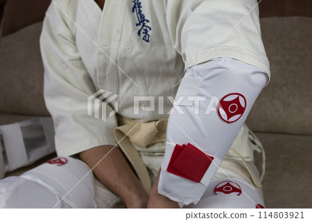Kyokushinkai karate athlete wears elbow protection, protective equipment for martial arts sparring, health protection in karate Kyokushinkai karate athlete wears elbow protection, protective equipment for martial arts sparring, health protection in karate 114803921