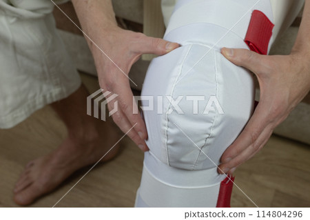 Kyokushinkai karate athlete adjusts protective equipment on his leg Kyokushinkai karate athlete adjusts protective equipment on his leg 114804296