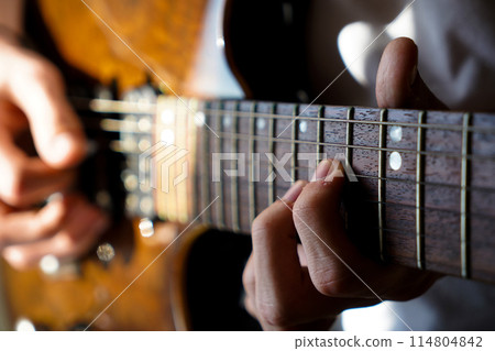 Hands of a Caucasian musician playing an electric guitar, playing a brown wooden electric guitar Hands of a Caucasian musician playing an electric guitar, playing a brown wooden electric guitar 114804842