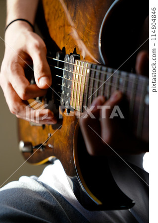 Hands of a Caucasian musician playing an electric guitar, playing a brown wooden electric guitar Hands of a Caucasian musician playing an electric guitar, playing a brown wooden electric guitar 114804846