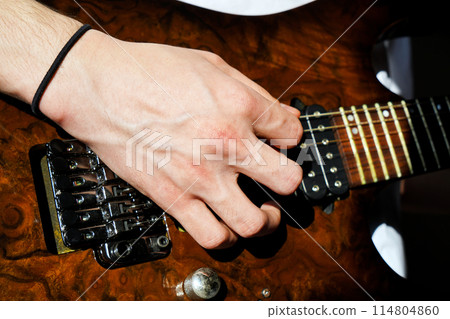 Hands of a Caucasian musician playing an electric guitar, playing a brown wooden electric guitar Hands of a Caucasian musician playing an electric guitar, playing a brown wooden electric guitar 114804860