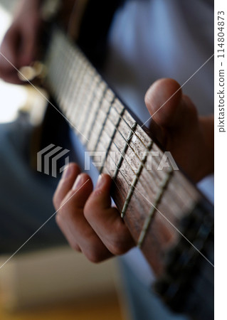 Hands of a Caucasian musician playing an electric guitar, playing a brown wooden electric guitar 114804873