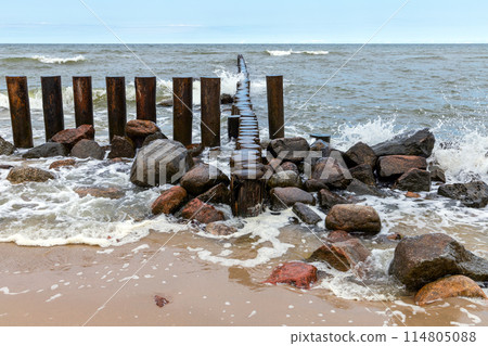 Concrete and wooden pillars as a parts of broken breakwater 114805088