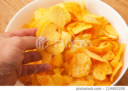 There are potato chips in a white plate, a caucasian person is holding potato chips in his hand 114805208