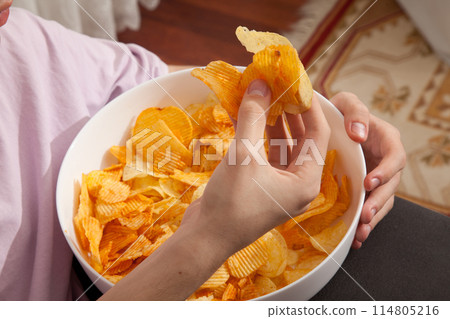Caucasian person in pink t-shirt holding plate full of potato chips and preparing to eat 114805216